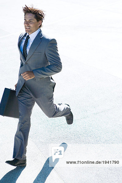 Young businessman running outdoors  carrying briefcase  full length