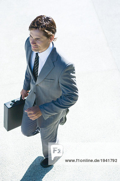 Young businessman walking outdoors  carrying briefcase  high angle view