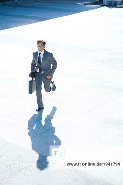 Young businessman running outdoors  carrying briefcase  full length