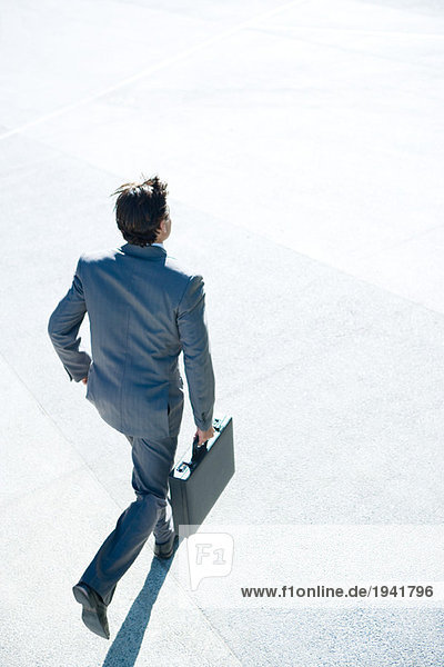 Young businessman running outdoors  carrying briefcase  rear view  high angle view