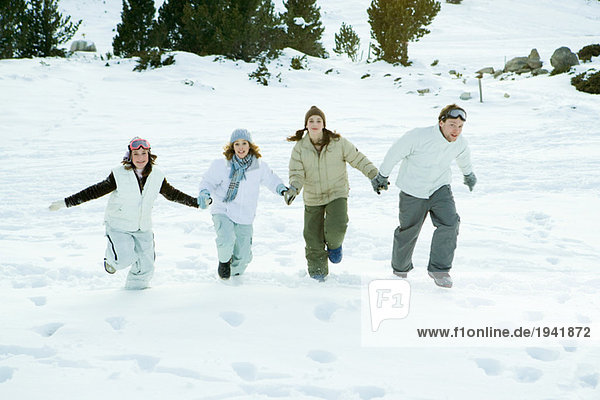 Vier junge Freunde  die zusammen im Schnee laufen  Händchen haltend  volle Länge