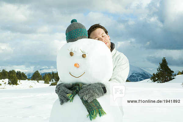 Young man embracing snowman  eyes closed  portrait