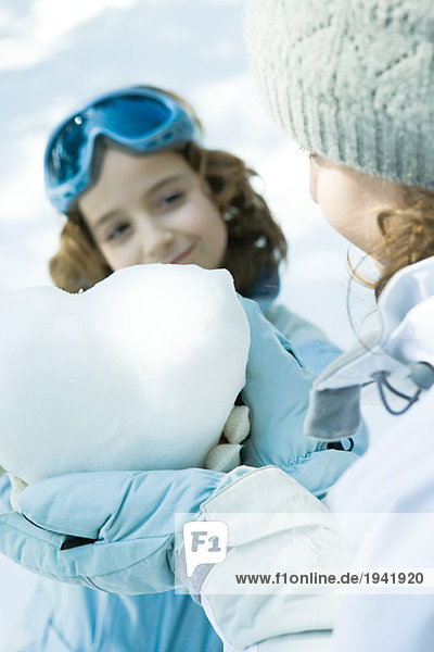 Teenagermädchen hält Herz aus Schnee  Schwester lächelt im Hintergrund