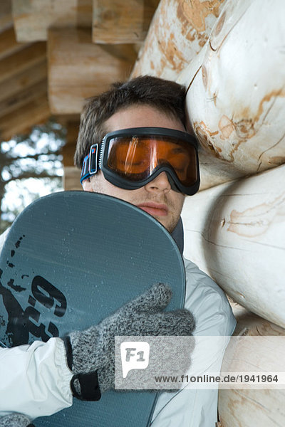 Young man holding snowboard  eyes closed  leaning against wall