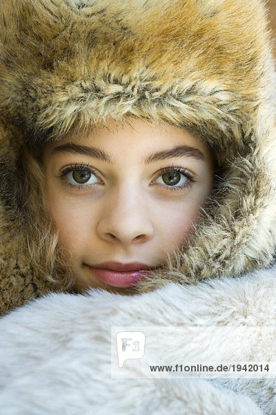 Preteen girl  wearing fur hat  wrapped in fur blanket  looking at camera  close-up portrait