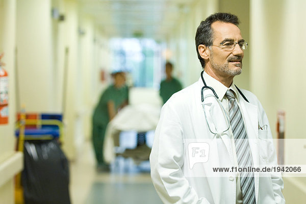 Männlicher Arzt schaut weg  lächelnd  Krankenhausflur im Hintergrund