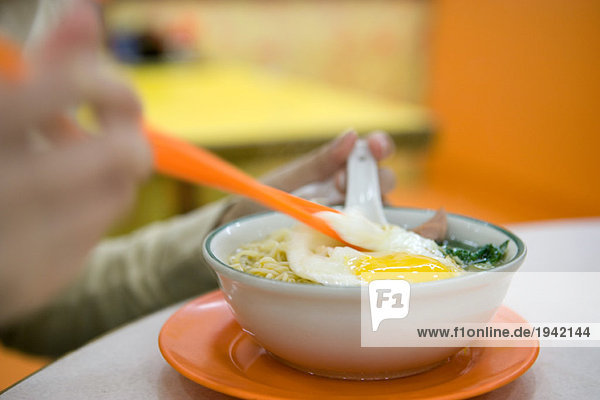 Person eating noodle dish with egg  cropped view