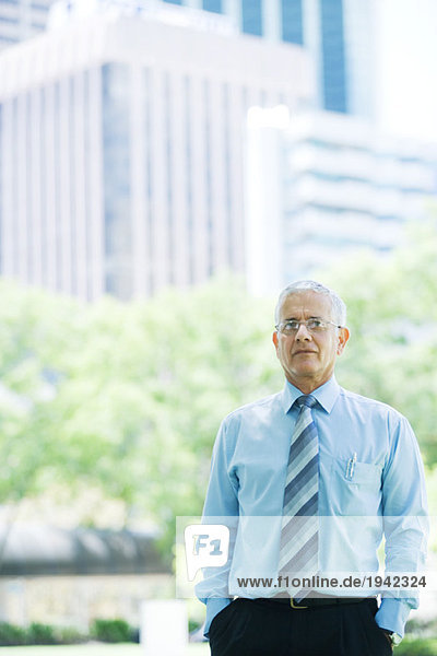 Geschäftsmann stehend mit Händen in den Taschen  Bürogebäude im Hintergrund  Portrait