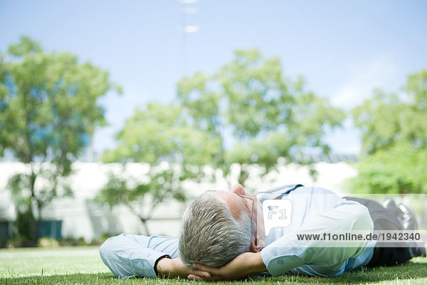 Businessman lying on grass  hands behind head