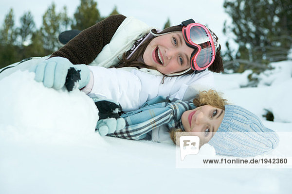 Zwei junge Freunde im Schnee liegend  lächelnd vor der Kamera  einer über dem anderen.