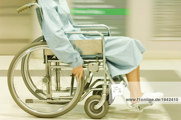 Abgeschnittener Blick auf den Menschen im Rollstuhl  im Krankenhausmantel  verschwommene Bewegung