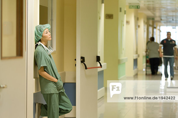 Krankenschwester im Krankenhaus  an die Wand gelehnt mit den Händen in den Taschen  Seitenansicht
