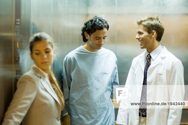 Männlicher Arzt im Gespräch mit Patient im Aufzug  Frau im Vordergrund