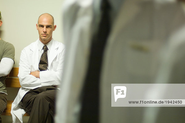 Männlicher Arzt sitzend mit gefalteten Armen  Blick auf die Kamera  Fokus auf den Hintergrund