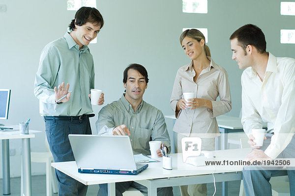 Vier Geschäftspartner im Büro  die auf den Laptop schauen und Kaffeetassen halten.