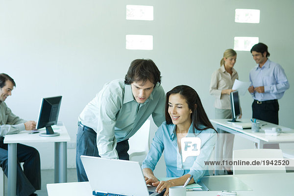 Geschäftsmann und Geschäftsfrau im Büro  mit Laptop  Mitarbeiter im Hintergrund