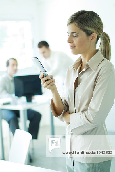 Young businesswoman in office  using cell phone  associates in background