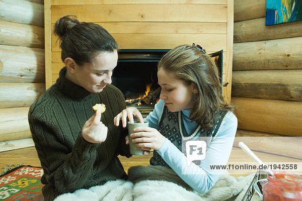Zwei jugendliche Mädchen sitzen am Kamin und teilen sich einen Snack.