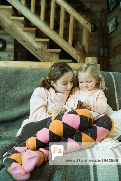 Mädchen und Kleinkind auf Couch sitzend  Lesebuch  volle Länge