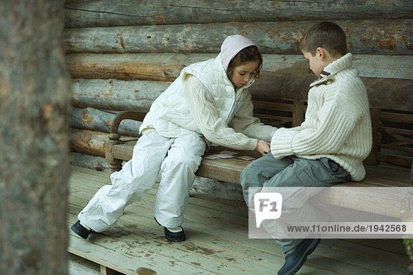 Mädchen und Junge spielen Karten im Freien  in Winterbekleidung