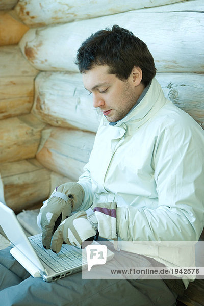 Junger Mann mit Laptop  Winterkleidung  Tippen mit Handschuhen