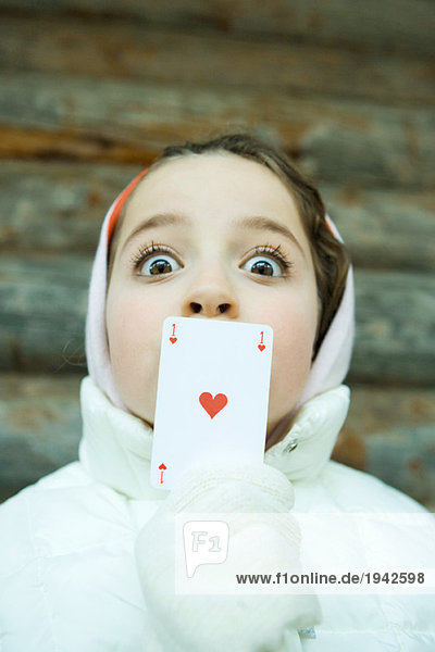 Mädchen mit Karte über dem Mund  gekleidet in Winterkleidung  Blick in die Kamera  große Augen