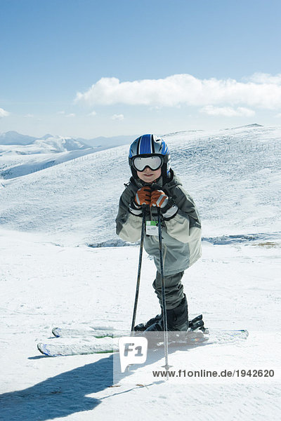 Junger Skifahrer  der sich auf Skistöcke stützt  lächelt in die Kamera  Ganzkörperporträt