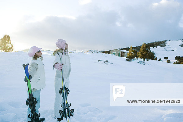Zwei junge Freunde stehen zusammen  halten Skier und schauen weg.