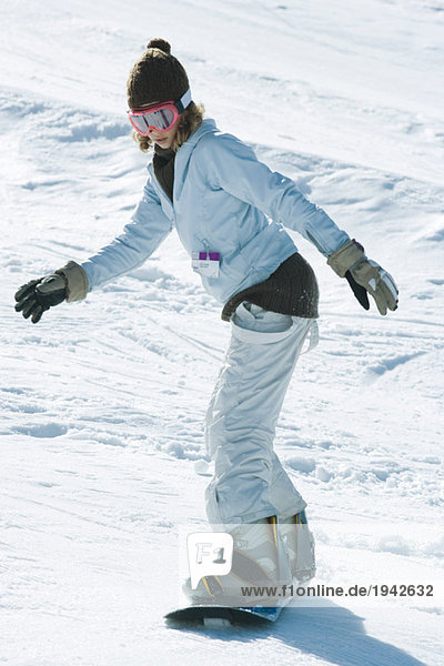Young female snowboarder on ski slope  side view  full length