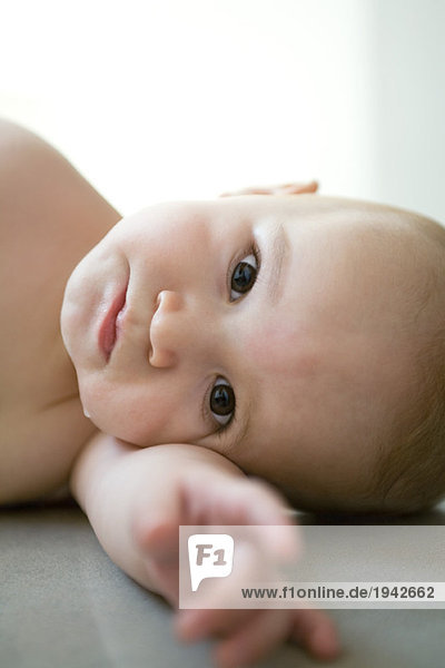 Baby schaut in die Kamera  der Kopf liegt auf dem Arm  auf der Seite.