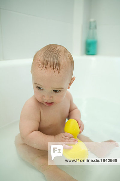 Nacktes Baby sitzend in der Badewanne  mit Badeente