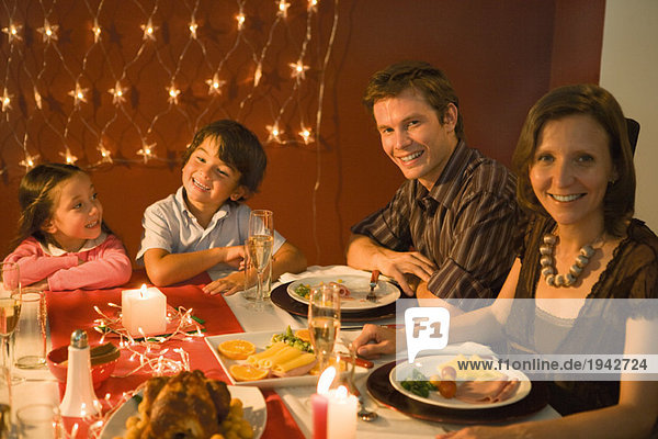 Familie mit zwei Kindern beim festlichen Abendessen  lächelnd vor der Kamera