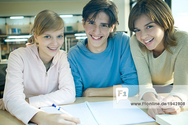 Drei Studenten studieren zusammen und lächeln vor der Kamera.