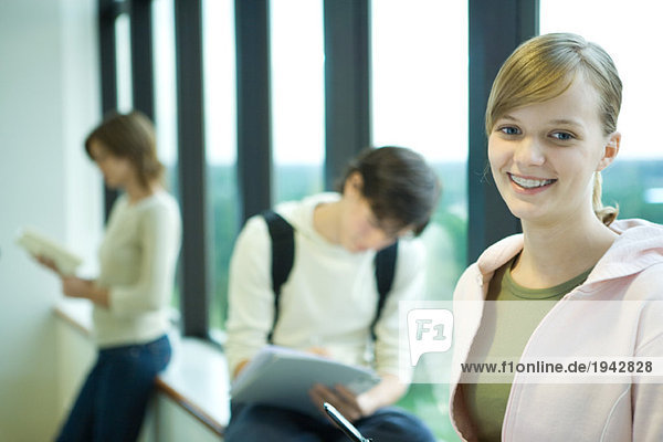 Studentin vor dem Fenster  lächelt in die Kamera  Peers im Hintergrund