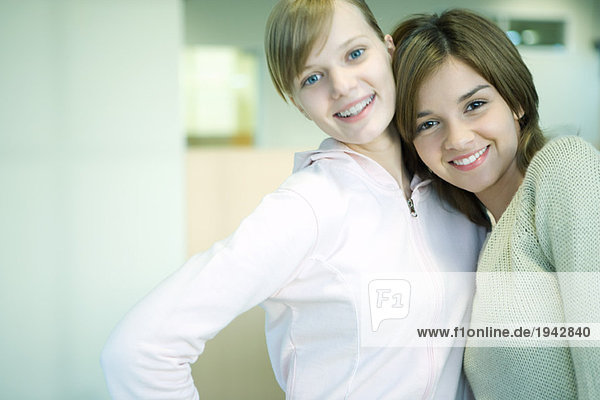 Zwei junge Freunde stehen zusammen  lächelnd  eine lehnt den Kopf auf die Schulter der anderen.