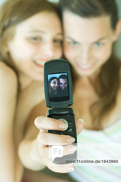 Teenage girl photographing self with friend using cell phone