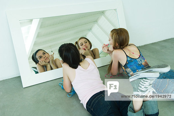 Zwei junge Freunde liegen auf dem Boden  halten Lippenstift  einer sieht sich selbst im Spiegel an.