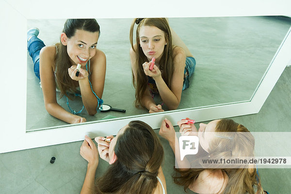 Zwei Freunde auf dem Boden liegend  Lippenstift auftragend  in den Spiegel schauend  einer in die Kamera schauend