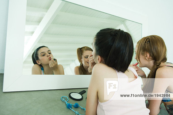 Zwei Freunde auf dem Boden liegend  Lippenstift auftragend  sich selbst im Spiegel betrachtend  Mund