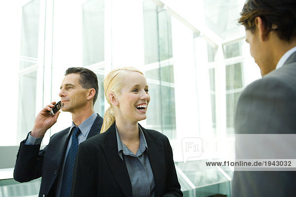 Geschäftskollegen im Flur  Frau lacht  Mann im Hintergrund mit Handy