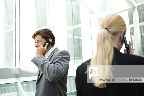 Business associates walking past each other in hallway  using cell phones