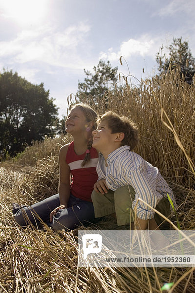 Junge und Mädchen (6-9) sitzen im Weizenfeld und schauen nach oben.