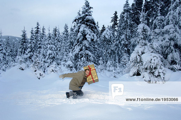 Young man carrying Christmas gift in snow  side view