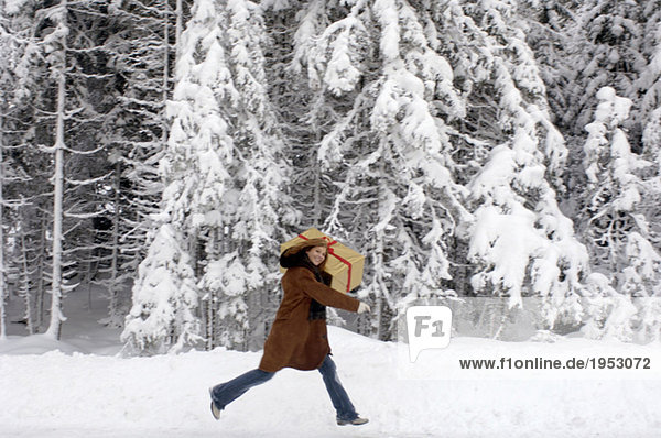 Junge Frau mit Weihnachtsgeschenk auf den Schultern im Schnee,  lächelnd