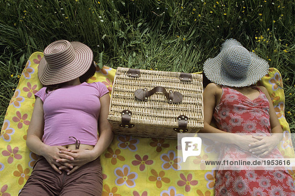 Frauen entspannen auf der Wiese mit Hut über dem Gesicht
