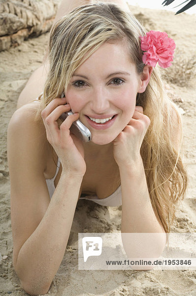 Junge Frau am Strand liegend mit dem Handy