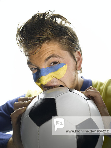 Junger Mann mit ukrainischer Flagge im Gesicht,  beißender Fußball,  Nahaufnahme