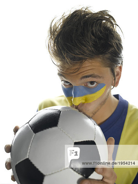 Junger Mann mit ukrainischer Flagge auf Gesicht gemalt  Fußball küssen  Portrait