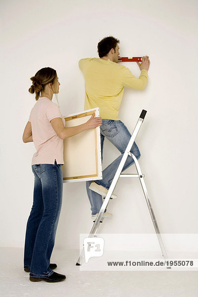 Young couple hanging up painting  man standing on ladder