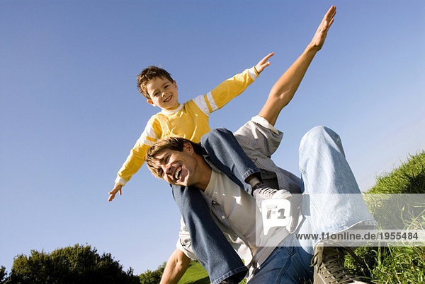 Boy (4-7) sitting on fathers shoulders  arms out